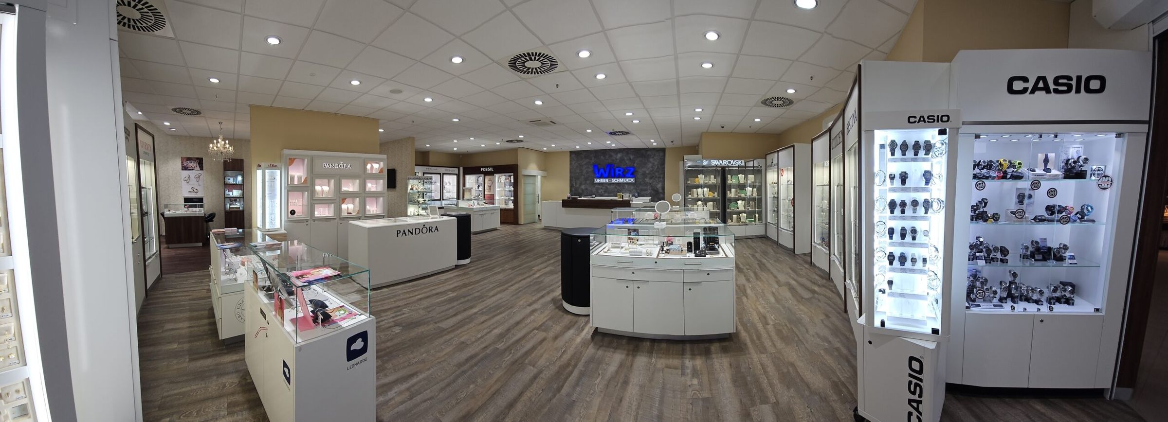 Innenansicht eines Uhren- und Schmuckgeschäfts mit mehreren beleuchteten Vitrinen und Holzfußboden.